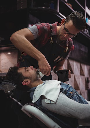 barber applying cream on clients beard in baber shop